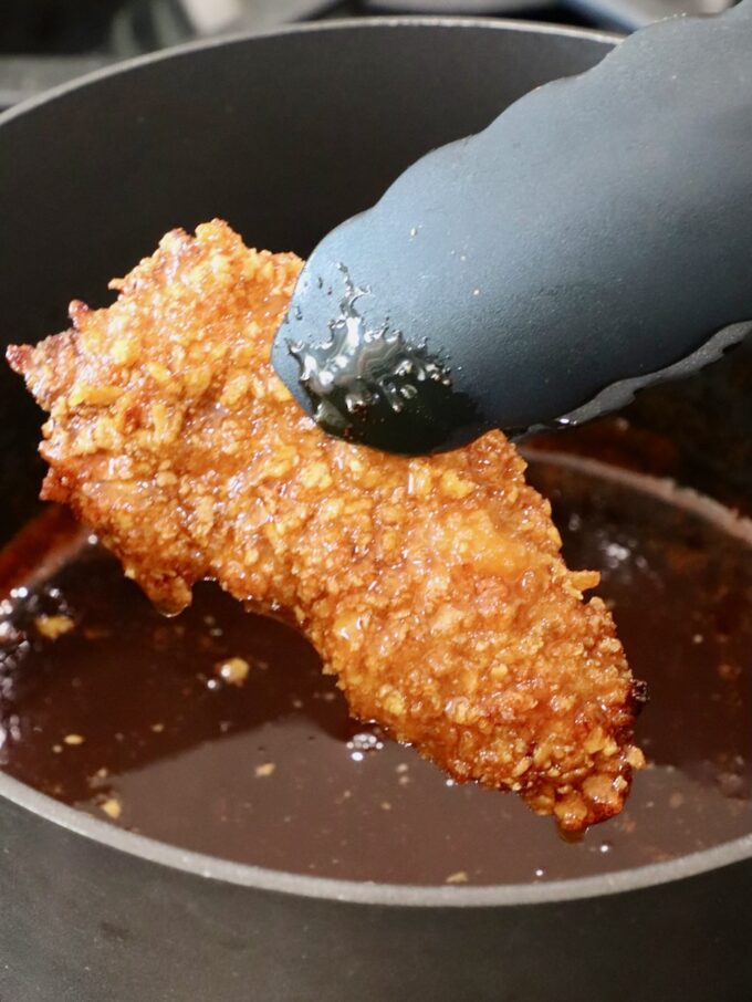 chicken dipped in the hot honey sauce held over the sauce with kitchen tongs