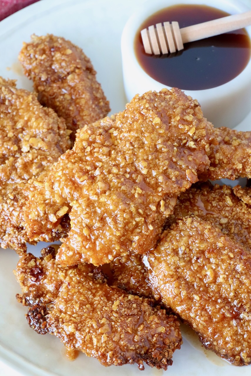 hot honey chicken tenders piled up on a plate with a bowl of hot honey sauce on the side