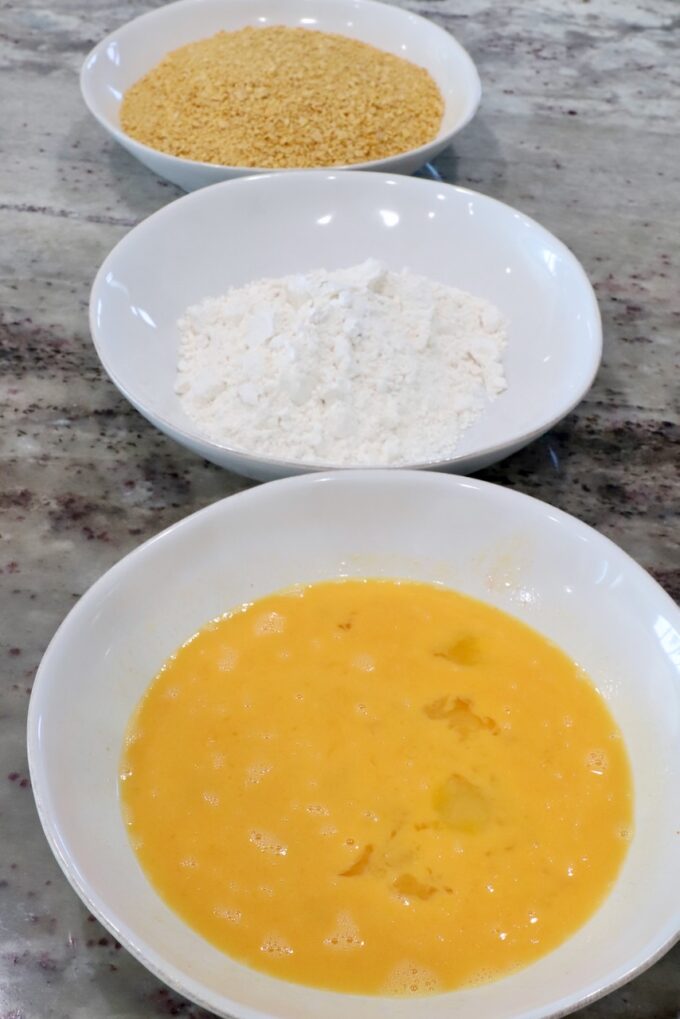 breading station with a bowl of egg wash, a bowl of flour and a bowl of crushed cornflakes