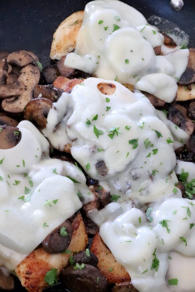 swiss cheese melted over cooked mushrooms on top of chicken in a skillet