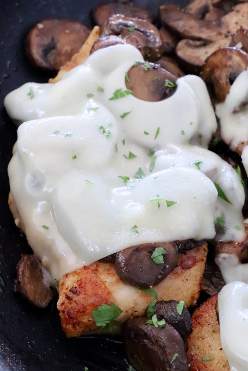 cooked chicken topped with mushrooms and melted swiss cheese in a skillet