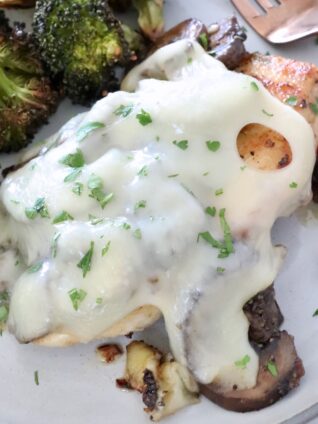 chicken covered in mushrooms and cheese on a plate with broccoli