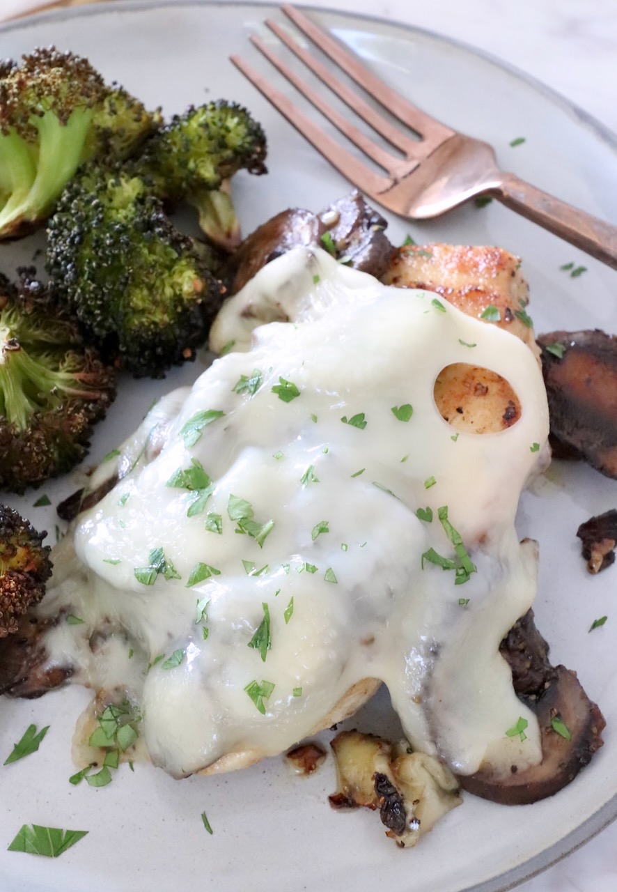 chicken topped with mushrooms and melted cheese on a plate with broccoli