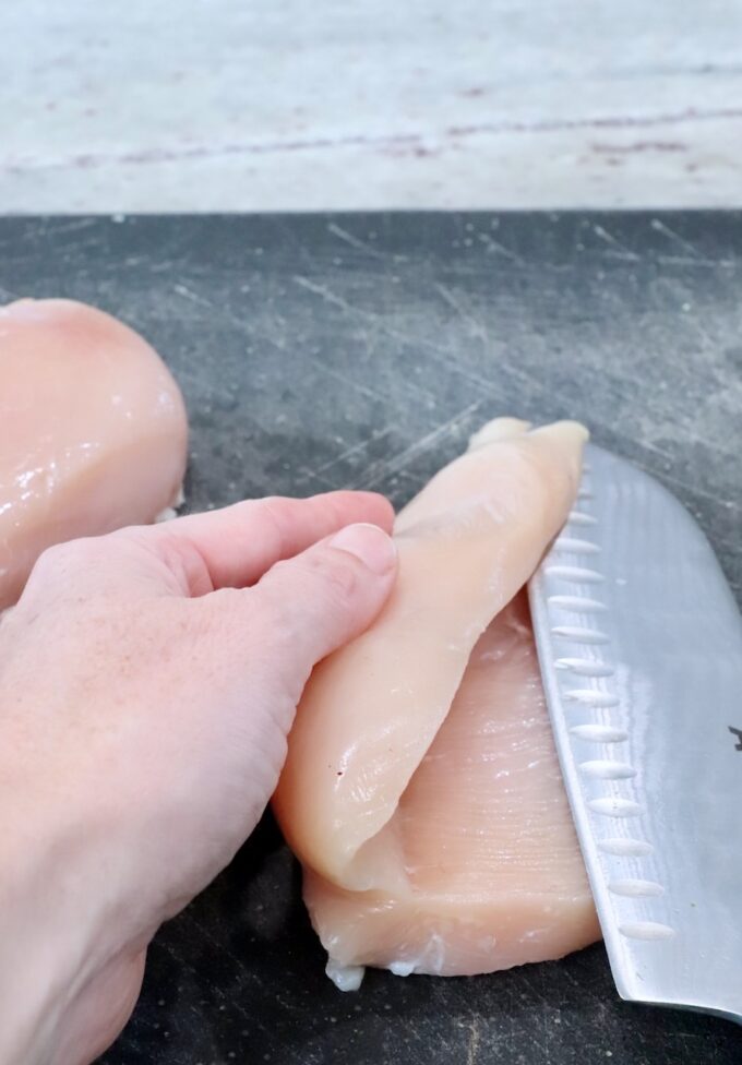 chicken sliced through the middle with a knife on a cutting board