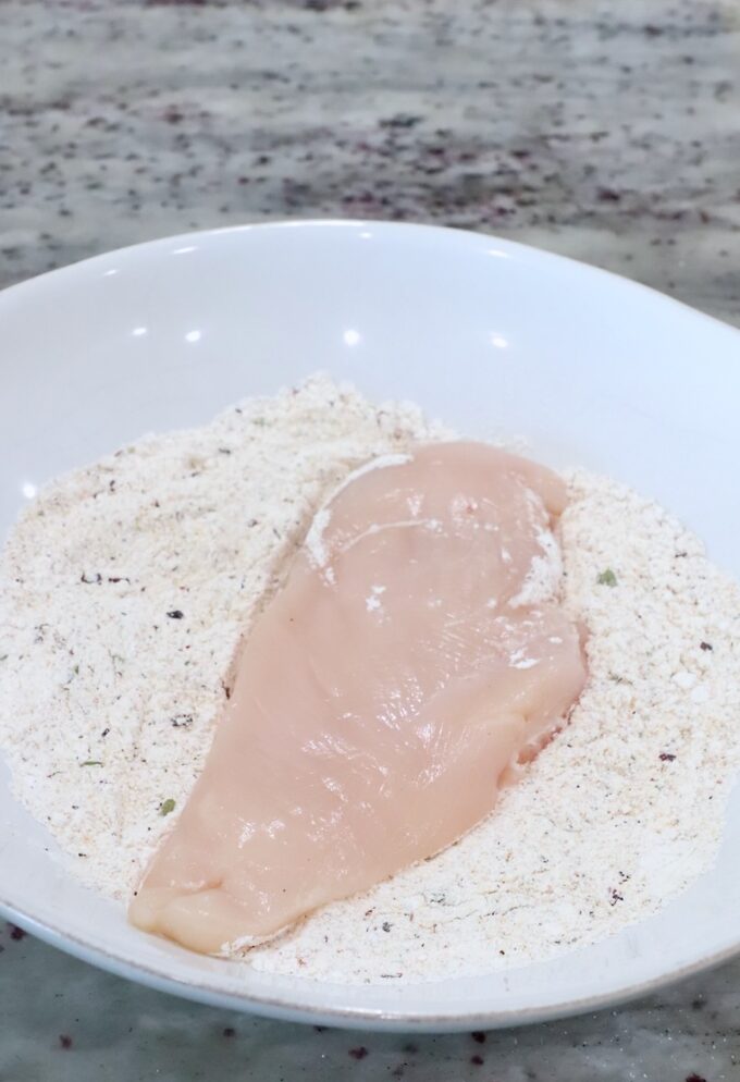 a chicken breast in a bowl of seasoned flour