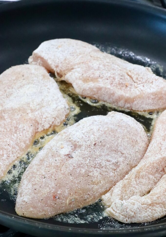 coated raw chicken breasts in a skillet with melted butter