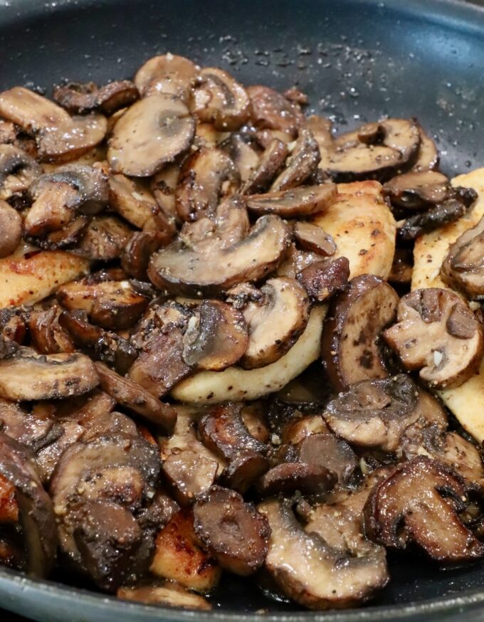 sauteed mushrooms on top of chicken breasts in a skillet