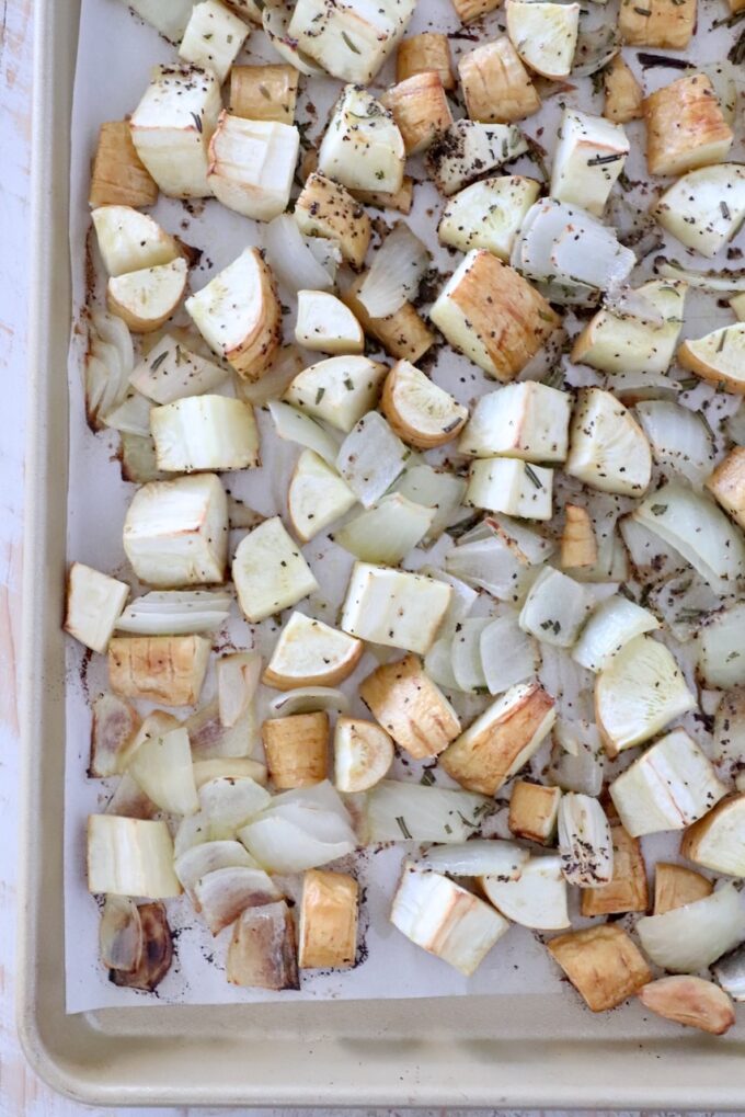 roasted diced parsnips on a baking sheet with onions, garlic and rosemary