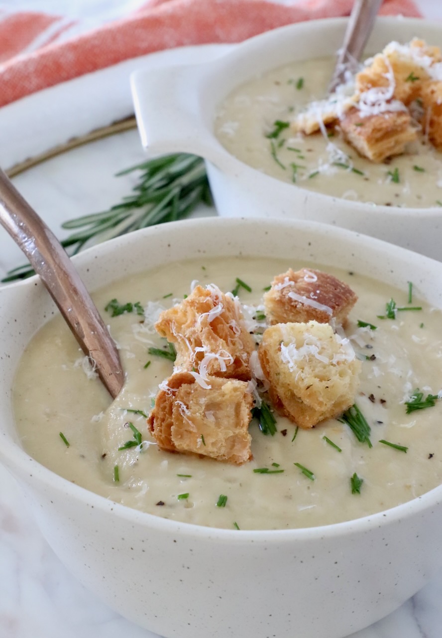 parsnip soup in a bowl topped with croutons and diced chives