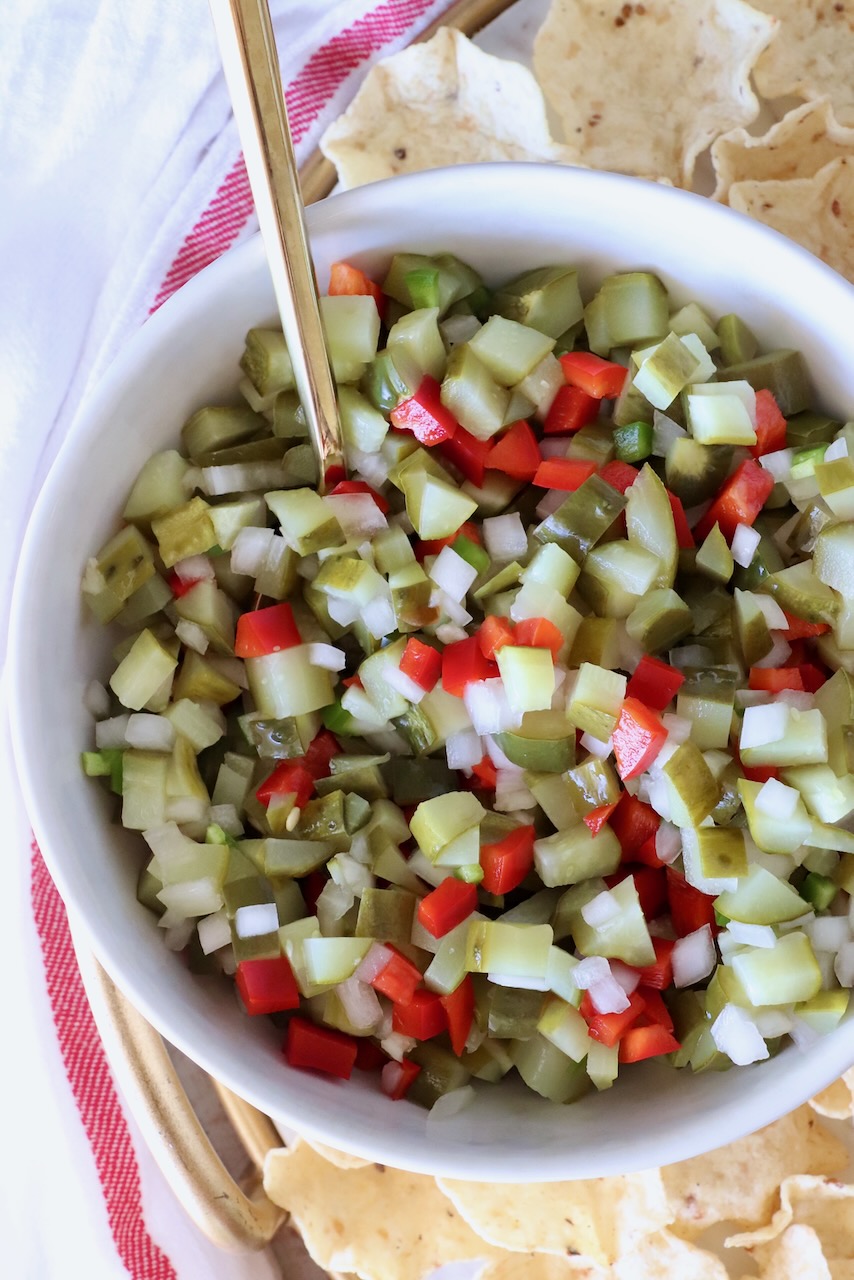 pickle de gallo in a bowl with a spoon surrounded by tortilla chips