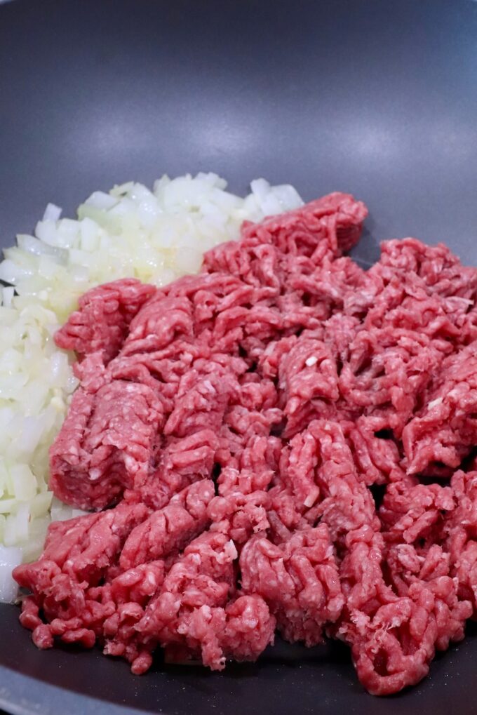 raw ground beef with diced onions in a large pot