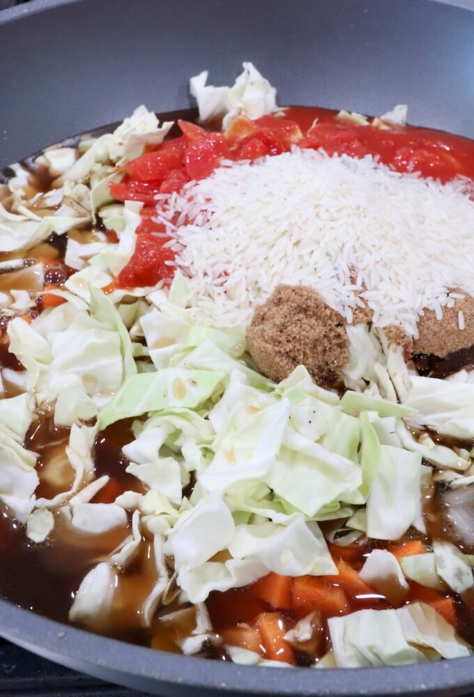 chopped cabbage, uncooked white rice and diced tomatoes in a large pot with cooked ground beef and onions