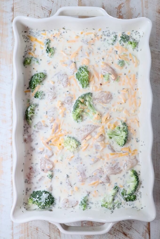 pieces of raw chicken and broccoli in a creamy sauce in a casserole dish