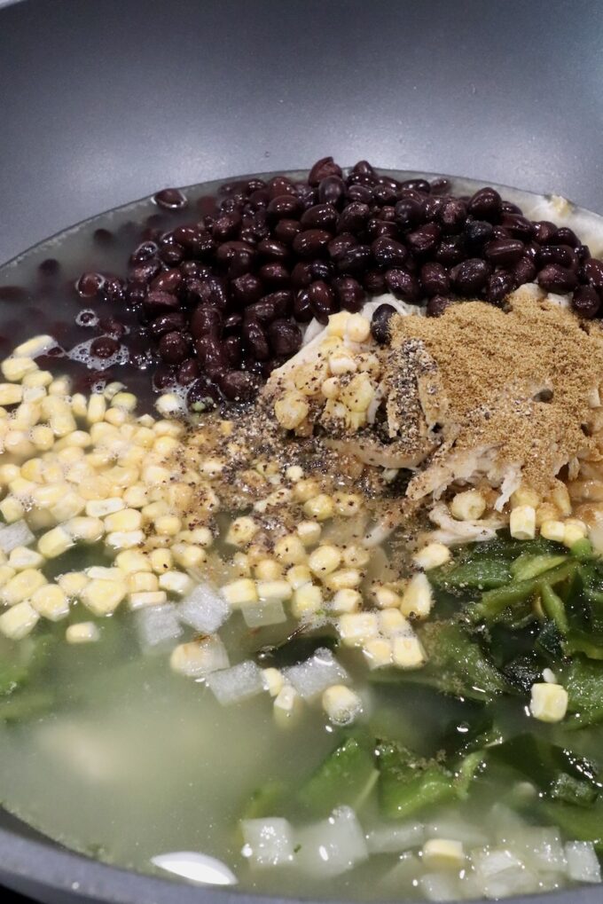 black beans, corn kernels, and roasted peppers in a large pot with spices