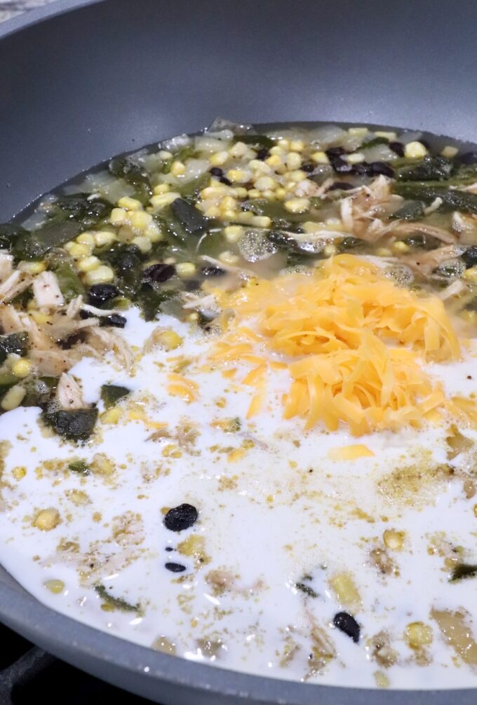 chicken poblano soup in a large pot with shredded cheddar cheese and heavy cream