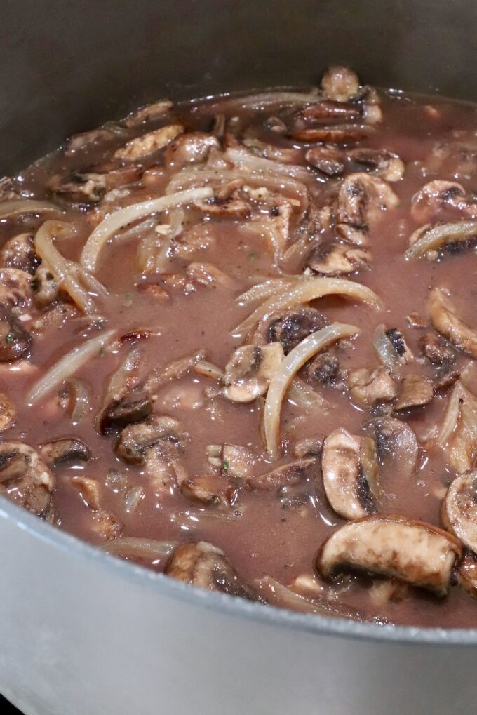 sliced onions and mushrooms in a red wine gravy in a large pot