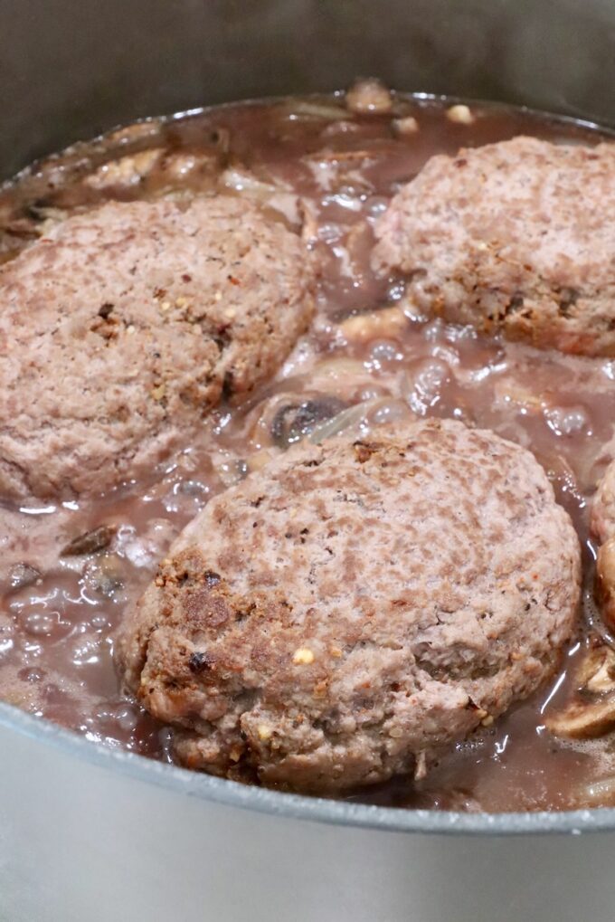 beef patties in pan with red wine gravy, mushrooms and onions