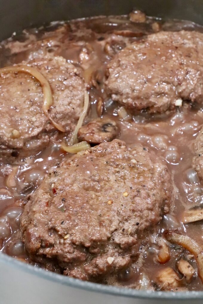 beef patties in pan with red wine gravy, mushrooms and onions