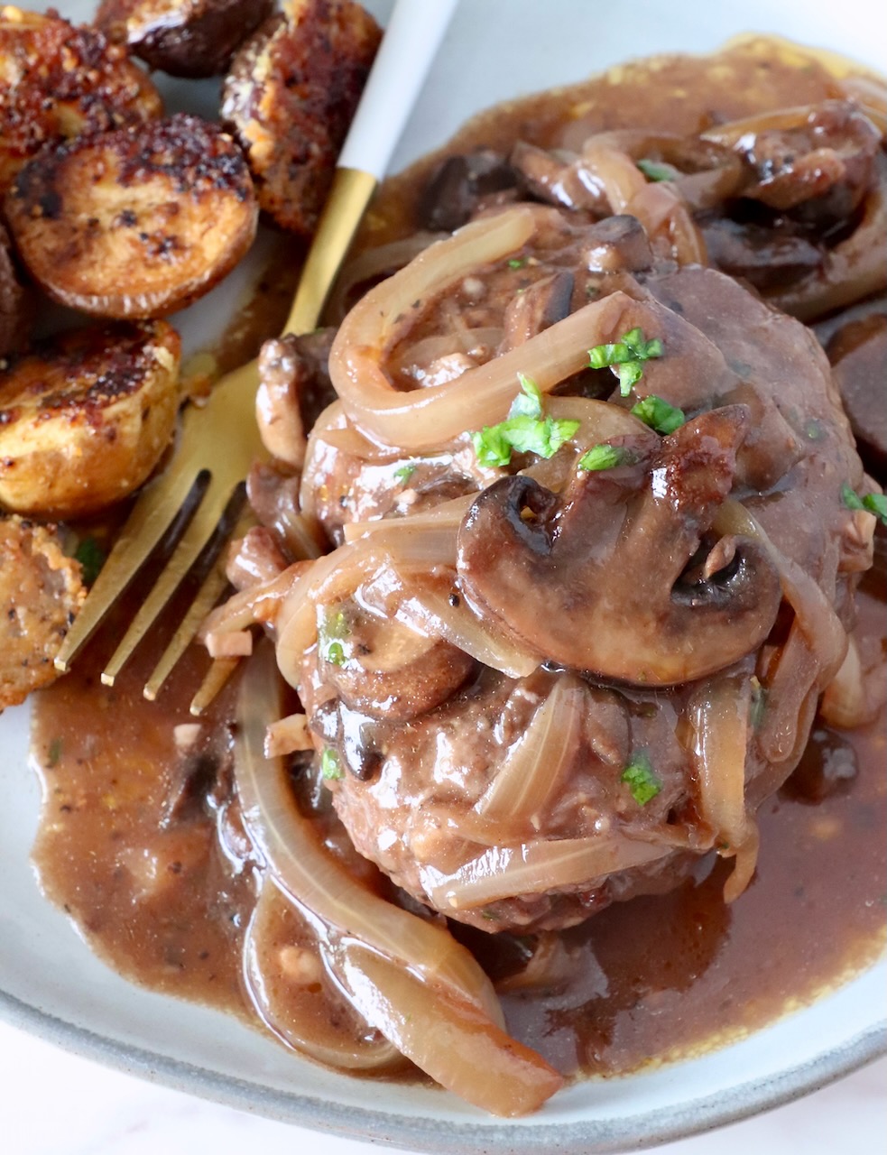 chopped steak on a plate with a fork covered with cooked sliced onions and mushrooms and gravy