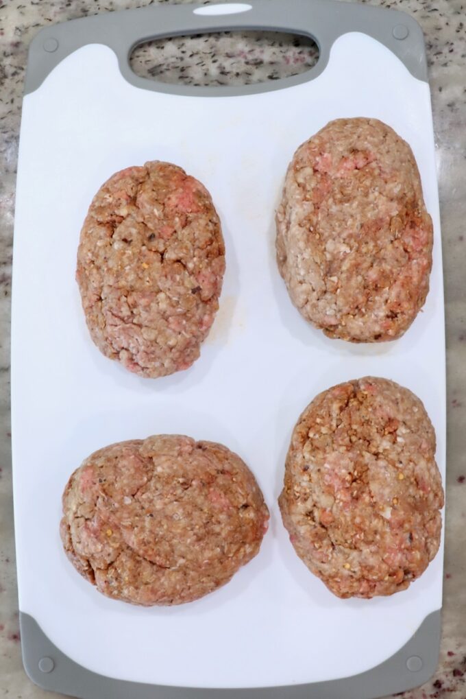 seasoned ground beef patties on a white cutting board