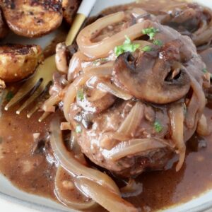 cooked chopped steak on a plate, covered with cooked, sliced onions and mushrooms and gravy