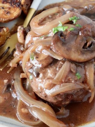 cooked chopped steak on a plate, covered with cooked, sliced onions and mushrooms and gravy