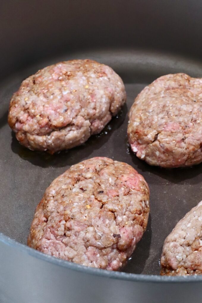 uncooked ground beef patties in a large dutch oven on the stove