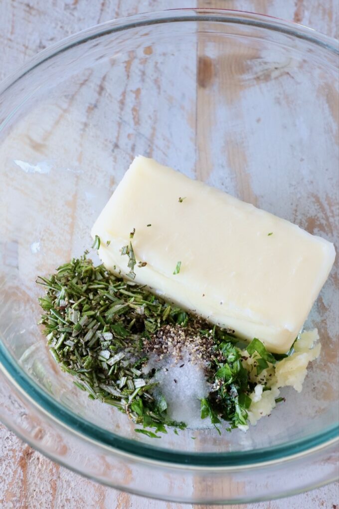 a stick of butter in a glass bowl with herbs, garlic and salt