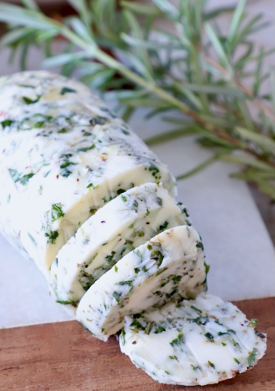 compound butter sliced on a cutting board with fresh rosemary on the side