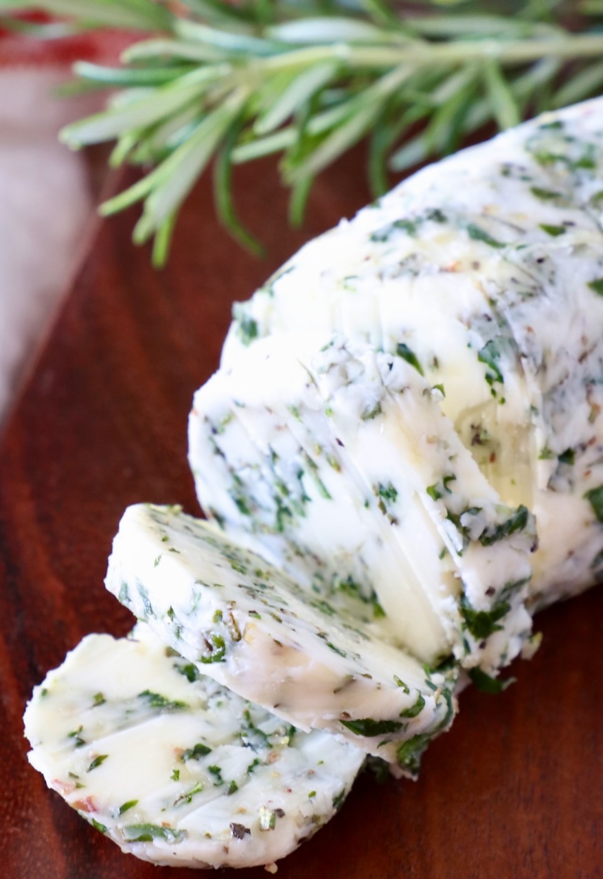 sliced herb butter on a wood cutting board with fresh rosemary