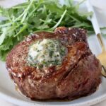 cooked filet mignon on a plate with herb butter on top