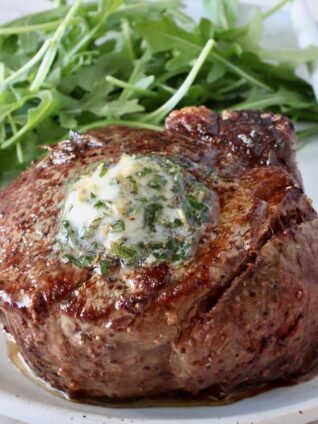 cooked filet mignon on a plate with herb butter on top