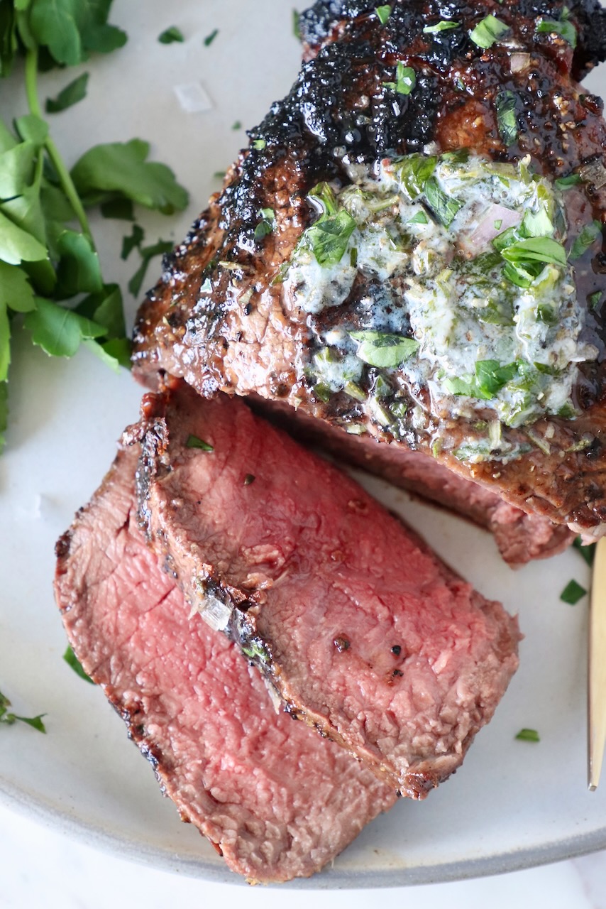 sliced, grilled filet mignon  on a plate, topped with melted herb butter