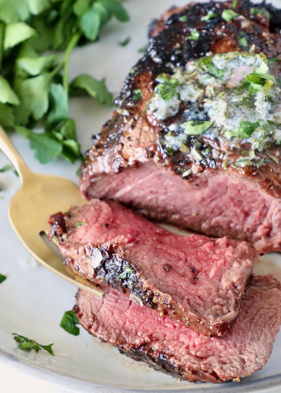 sliced filet mignon steak on a plate with a fork and fresh parsley