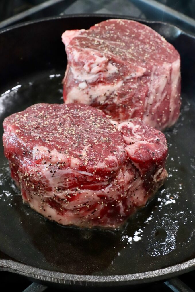 seasoned filet mignon steaks in a cast iron skillet on the stove