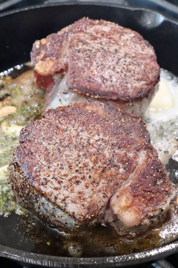 seared steaks in a cast iron skillet on the stove with butter and garlic