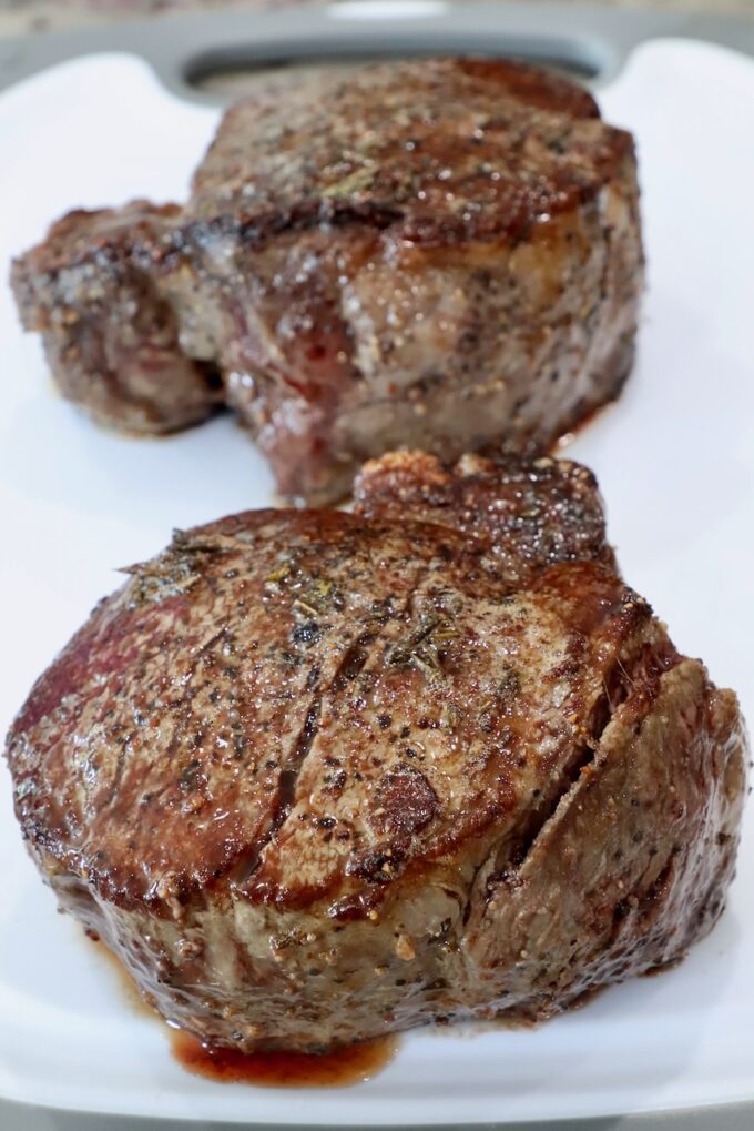 two cooked filet mignon steaks resting on a white cutting board