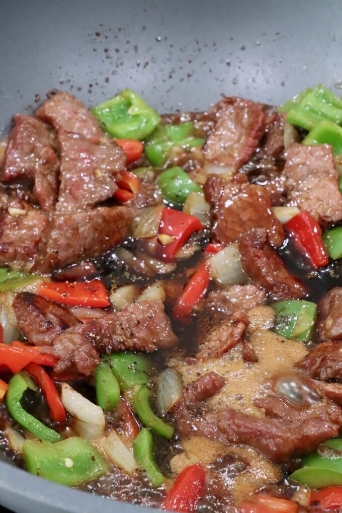 cooked beef, diced bell peppers and onions mixed together in a large wok with sauce