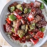 cooked steak and peppers in sauce over cooked white rice in a bowl topped with sesame seeds