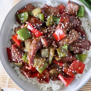 cooked steak and peppers in sauce over cooked white rice in a bowl topped with sesame seeds