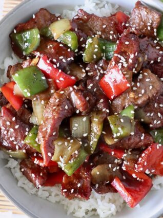 cooked steak and peppers in sauce over cooked white rice in a bowl topped with sesame seeds