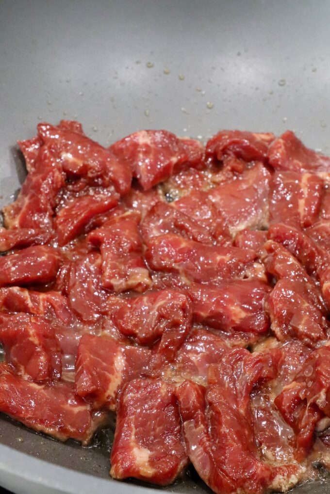 marinated strips of uncooked beef in a wok