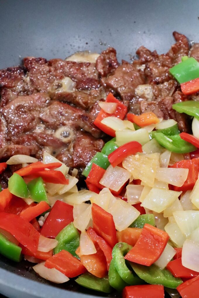 cooked beef, diced bell peppers and onions in a large wok