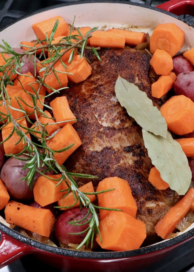 seared pork shoulder in a large pot with diced carrots, potatoes, bay leaves and rosemary