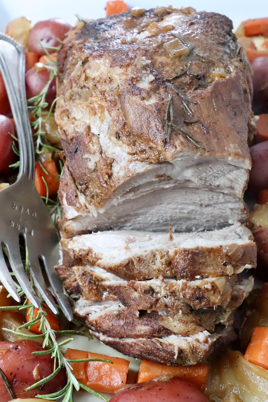 pork roast partially sliced on a serving plate with a large fork and roasted vegetables