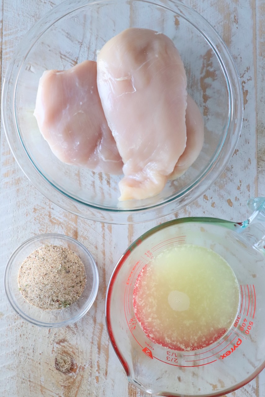 three glass bowls filled with raw chicken breasts, chicken seasoning and chicken broth