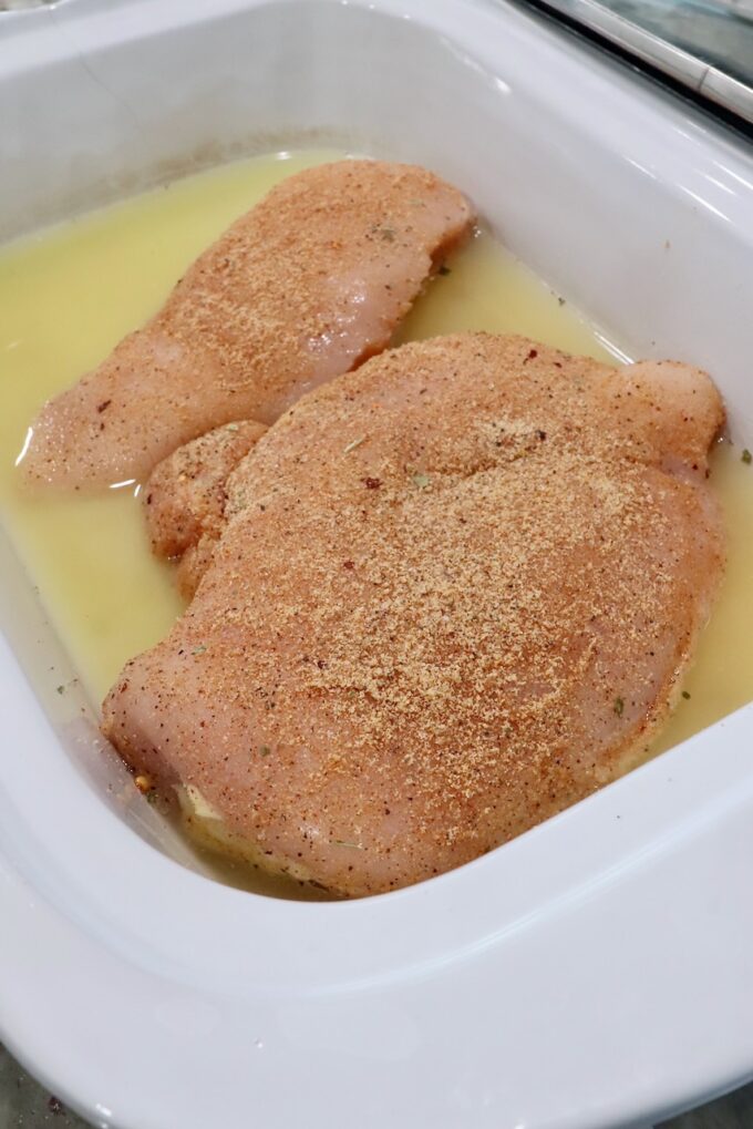 raw seasoned chicken breasts in a slow cooker with chicken broth