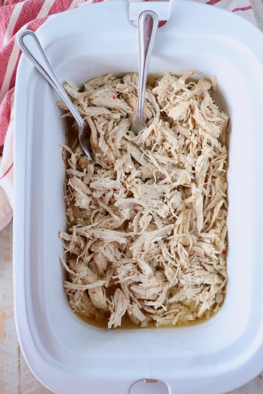 cooked shredded chicken breasts in a slow cooker with two forks