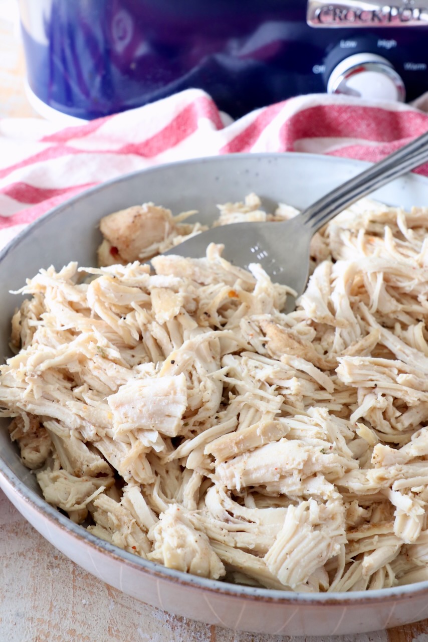 shredded chicken in a bowl in front of a Crock Pot