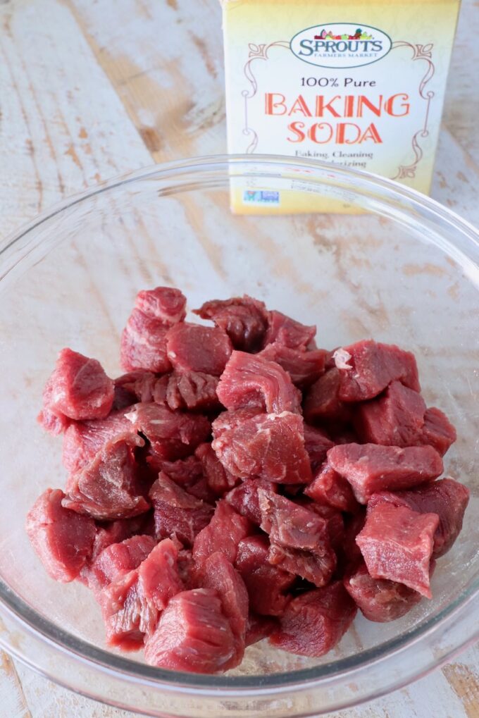 cubes of sirloin steak in a glass bowl with a box of baking soda behind it